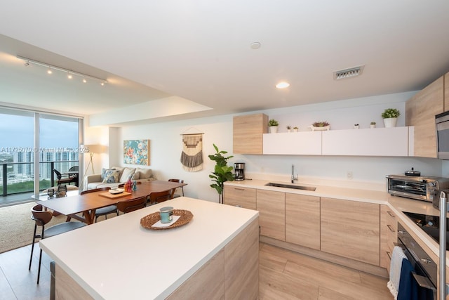 kitchen featuring black electric stovetop, a center island, floor to ceiling windows, light brown cabinetry, and sink