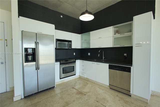 kitchen featuring pendant lighting, stainless steel appliances, dark countertops, white cabinets, and a sink