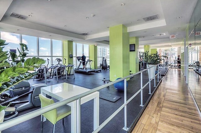 gym featuring expansive windows, visible vents, a raised ceiling, and wood finished floors