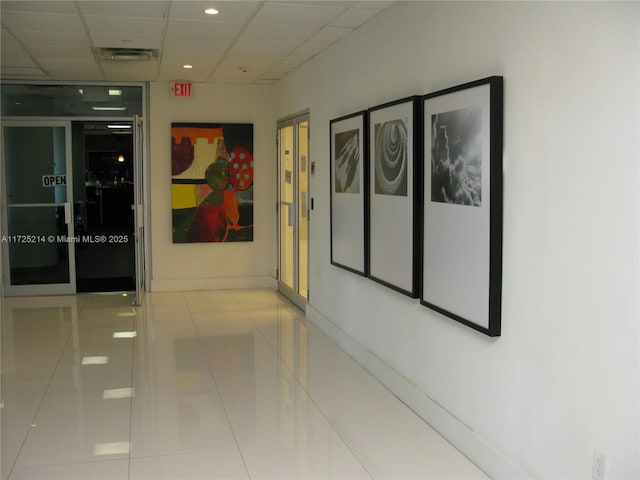 hall with light tile patterned flooring and a drop ceiling