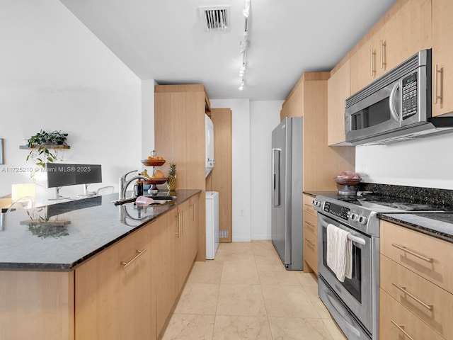 kitchen with light brown cabinetry, rail lighting, dark stone counters, appliances with stainless steel finishes, and sink