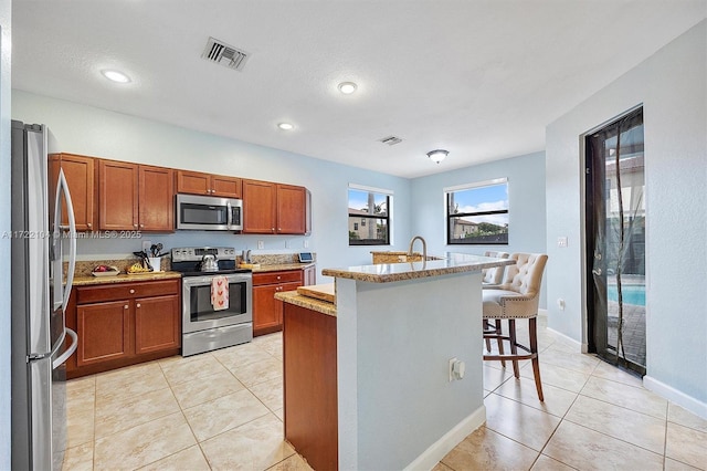 kitchen featuring stainless steel appliances, light tile patterned floors, a kitchen breakfast bar, and a kitchen island with sink