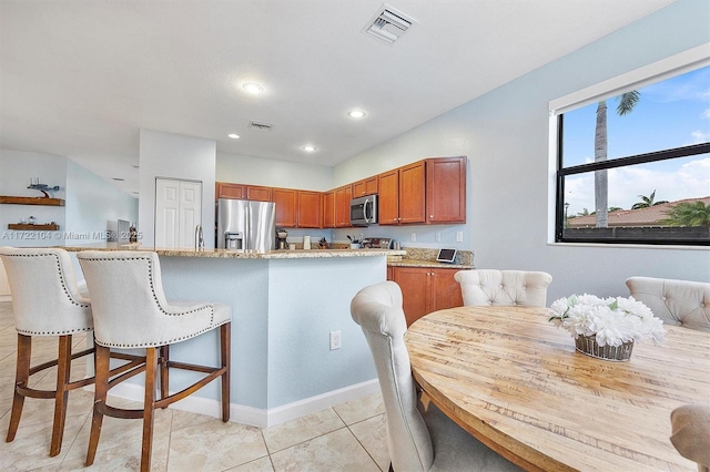 kitchen with light stone counters, stainless steel appliances, light tile patterned floors, and a kitchen breakfast bar