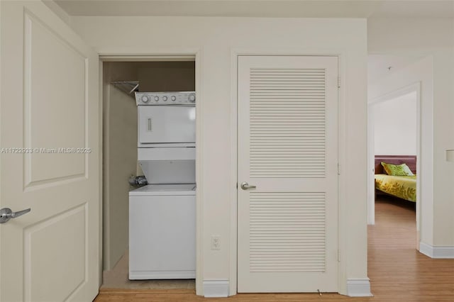 laundry room with hardwood / wood-style flooring and stacked washer and clothes dryer