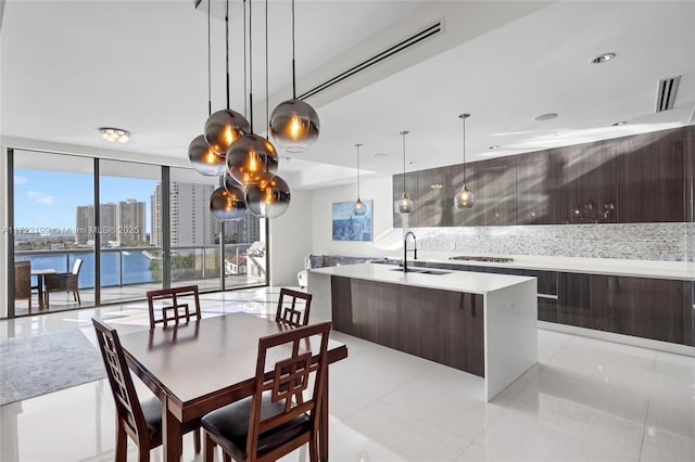 kitchen featuring a center island with sink, a water view, floor to ceiling windows, decorative light fixtures, and sink