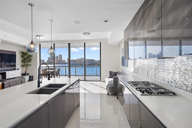 kitchen with decorative light fixtures, sink, light tile patterned floors, tasteful backsplash, and a water view