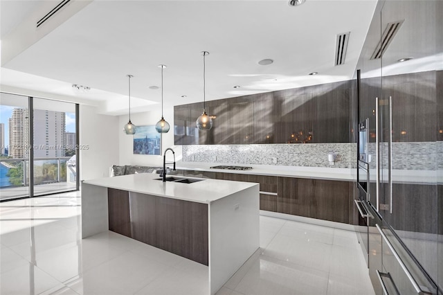 kitchen with a kitchen island with sink, light tile patterned floors, hanging light fixtures, and sink