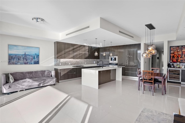 kitchen with beverage cooler, a center island with sink, pendant lighting, sink, and light tile patterned flooring