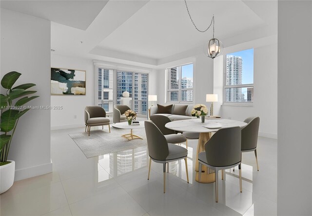 tiled dining room featuring a notable chandelier and a raised ceiling