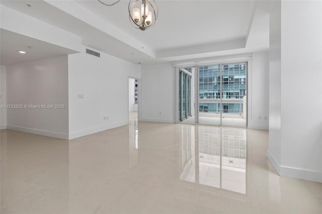 tiled empty room featuring a tray ceiling, a notable chandelier, and floor to ceiling windows