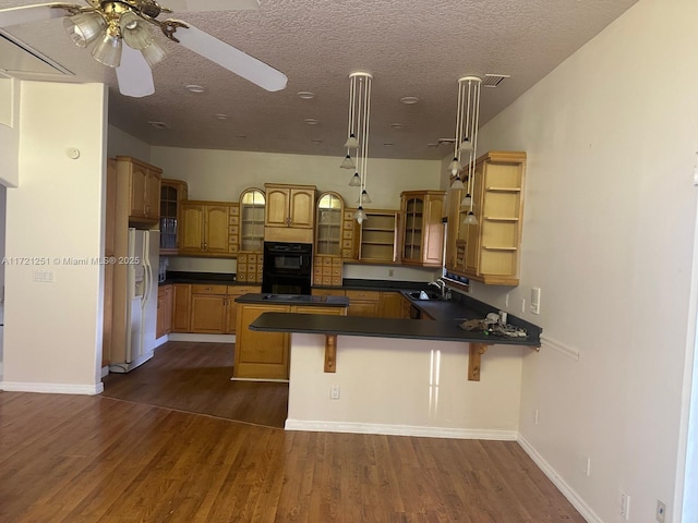 kitchen with ceiling fan, dark hardwood / wood-style floors, double oven, a breakfast bar, and white refrigerator with ice dispenser