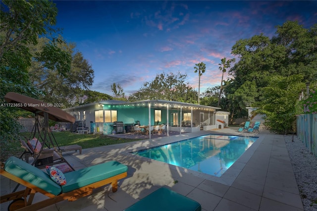 pool at dusk featuring a patio and a grill