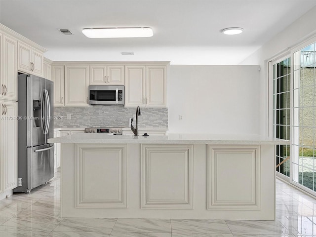 kitchen featuring stainless steel appliances, a center island with sink, a healthy amount of sunlight, and cream cabinetry