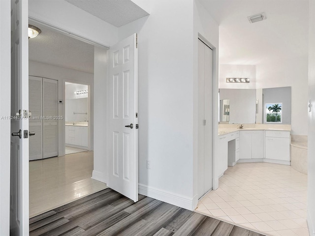 hallway with sink, a textured ceiling, and light wood-type flooring