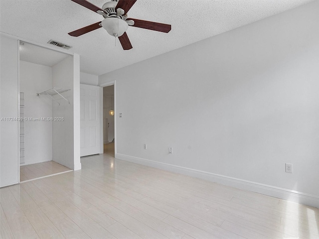 unfurnished bedroom featuring a walk in closet, a textured ceiling, ceiling fan, and a closet