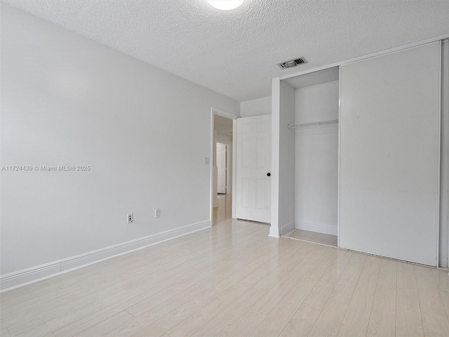 unfurnished bedroom featuring a textured ceiling, light hardwood / wood-style floors, and a closet