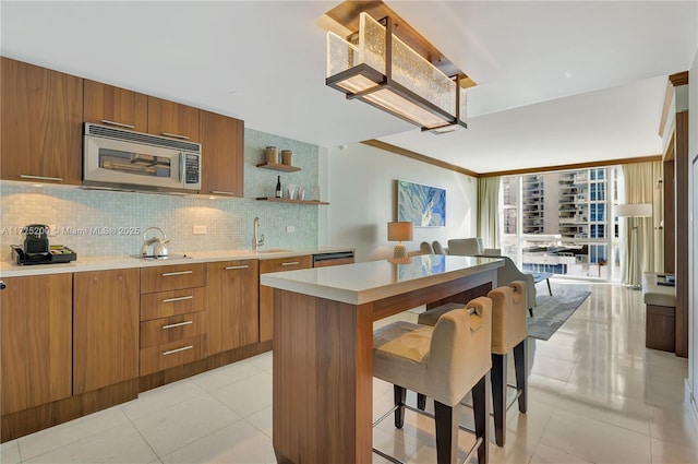 kitchen featuring stainless steel appliances, light tile patterned floors, decorative backsplash, a kitchen island, and sink