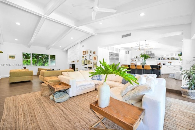 living room with a brick fireplace, lofted ceiling with beams, ceiling fan with notable chandelier, and hardwood / wood-style flooring