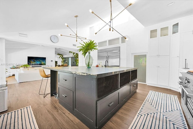 kitchen with white cabinets, pendant lighting, light stone countertops, high quality appliances, and a kitchen island with sink