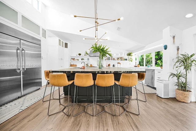 kitchen with stainless steel appliances, a notable chandelier, light hardwood / wood-style floors, a breakfast bar, and white cabinetry