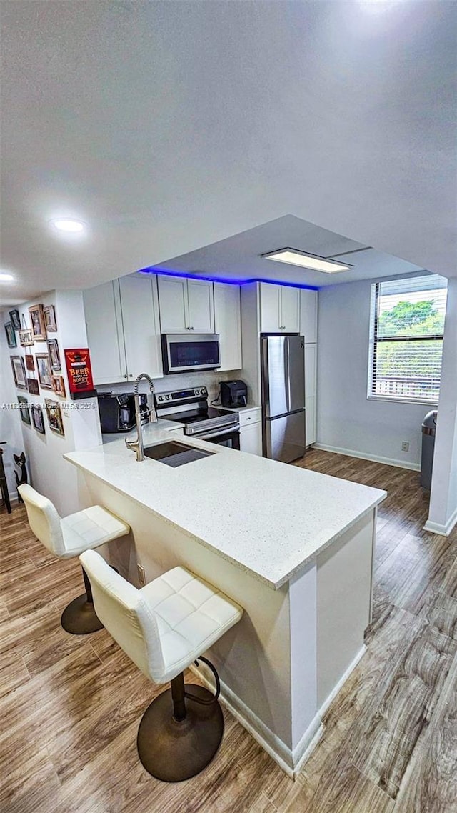 kitchen featuring stainless steel appliances, a kitchen breakfast bar, light hardwood / wood-style flooring, and kitchen peninsula