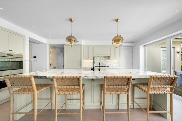 kitchen featuring tasteful backsplash, a breakfast bar, light stone counters, and decorative light fixtures