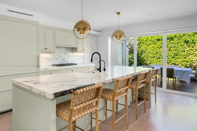 kitchen with a large island with sink, tasteful backsplash, hanging light fixtures, and gas cooktop