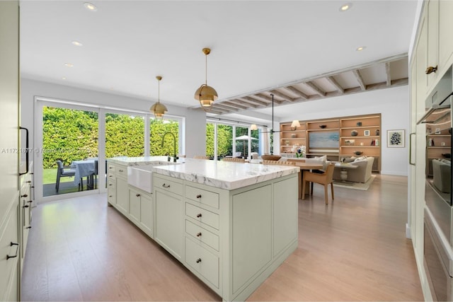 kitchen with pendant lighting, sink, light stone counters, an island with sink, and beamed ceiling