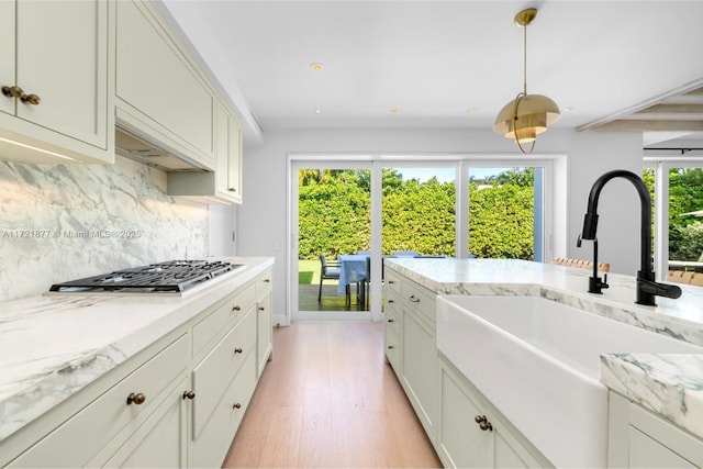 kitchen with pendant lighting, stainless steel gas stovetop, sink, decorative backsplash, and light stone countertops