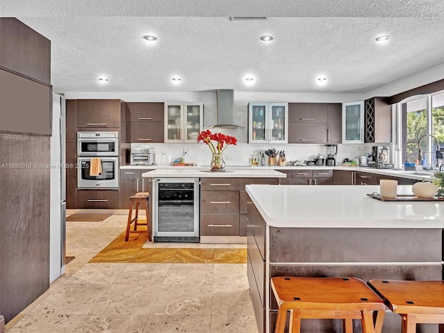 kitchen featuring a large island, beverage cooler, double oven, a breakfast bar, and wall chimney range hood