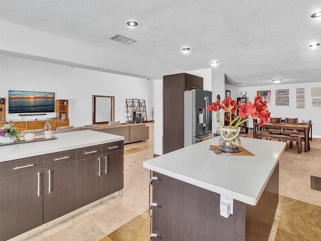 kitchen with a textured ceiling, a center island, high quality fridge, and dark brown cabinetry