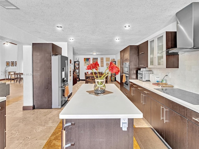 kitchen with a center island, wall chimney exhaust hood, decorative backsplash, black electric cooktop, and stainless steel fridge