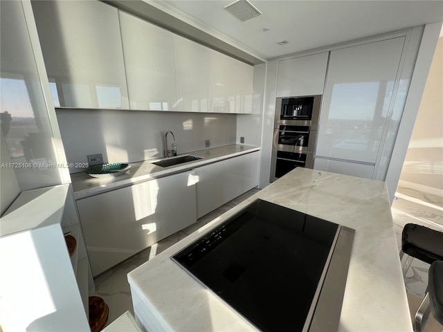 kitchen featuring sink, white cabinetry, stainless steel double oven, and light stone countertops