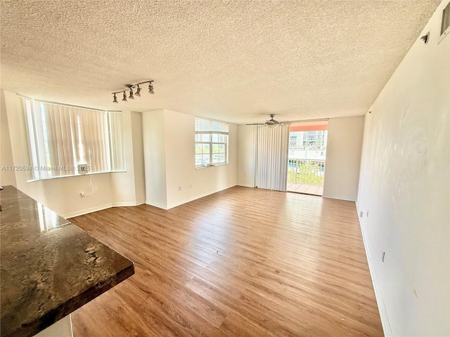 empty room with ceiling fan, track lighting, a textured ceiling, and hardwood / wood-style floors