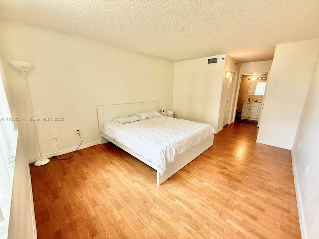 unfurnished bedroom featuring ensuite bath, wood-type flooring, and a textured ceiling