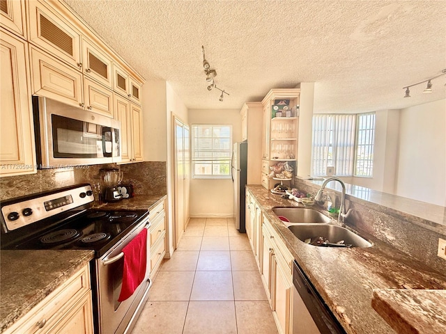 kitchen with stainless steel appliances, dark stone countertops, sink, cream cabinets, and light tile patterned flooring