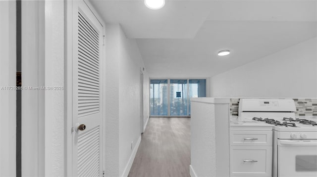 kitchen with light wood-type flooring, white range with gas stovetop, tasteful backsplash, and white cabinetry