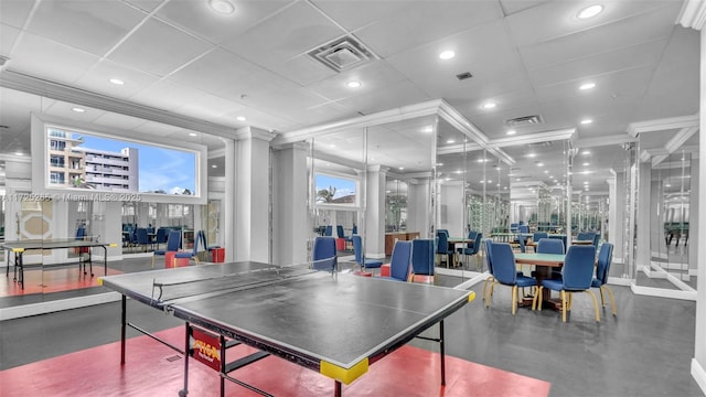 rec room featuring a drop ceiling, concrete floors, crown molding, and decorative columns