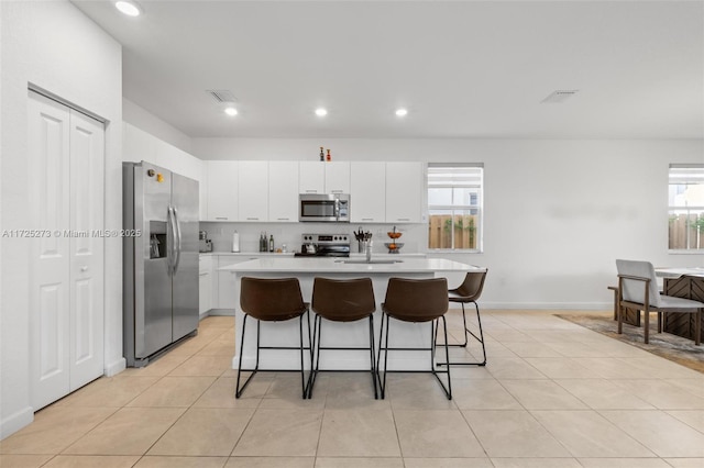 kitchen with a kitchen island with sink, appliances with stainless steel finishes, a breakfast bar, white cabinetry, and light tile patterned flooring