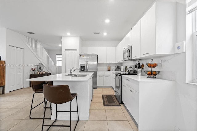 kitchen featuring stainless steel appliances, white cabinets, a breakfast bar, light tile patterned flooring, and a kitchen island with sink