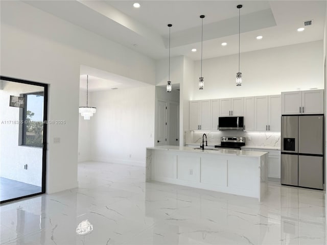 kitchen with white cabinets, a raised ceiling, appliances with stainless steel finishes, and hanging light fixtures