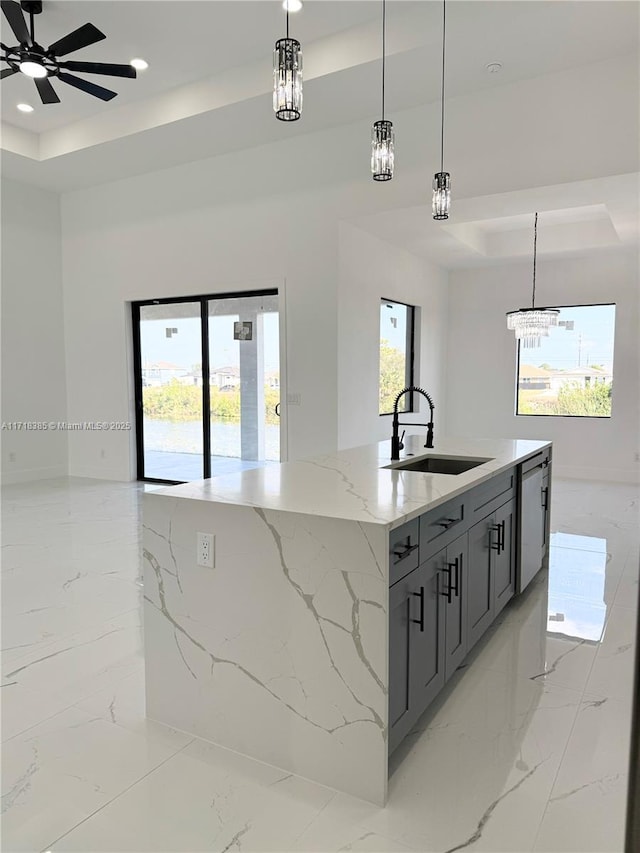 kitchen featuring sink, a center island with sink, a raised ceiling, and pendant lighting