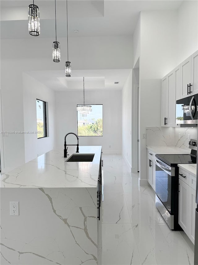 kitchen featuring light stone counters, a center island with sink, white cabinetry, appliances with stainless steel finishes, and sink