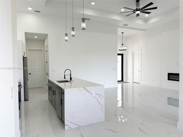 kitchen featuring sink, ceiling fan, light stone countertops, a center island with sink, and pendant lighting