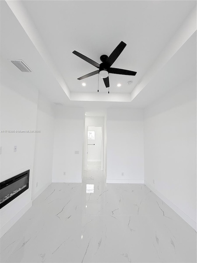 unfurnished living room featuring ceiling fan and a tray ceiling