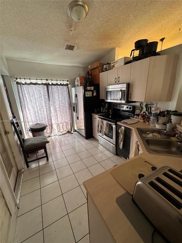 kitchen with appliances with stainless steel finishes, a textured ceiling, sink, and light tile patterned floors