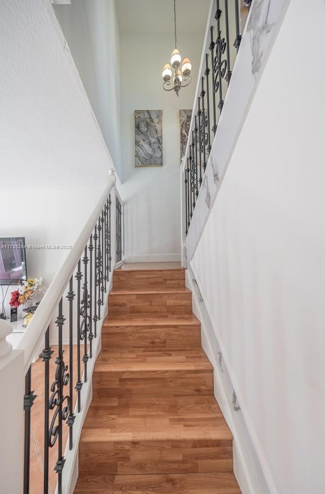 stairs featuring a towering ceiling, a chandelier, and wood-type flooring