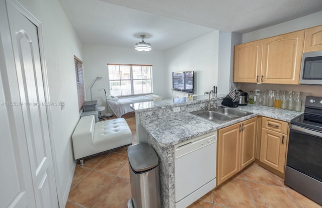 kitchen with stainless steel appliances, sink, light tile patterned floors, kitchen peninsula, and light brown cabinetry