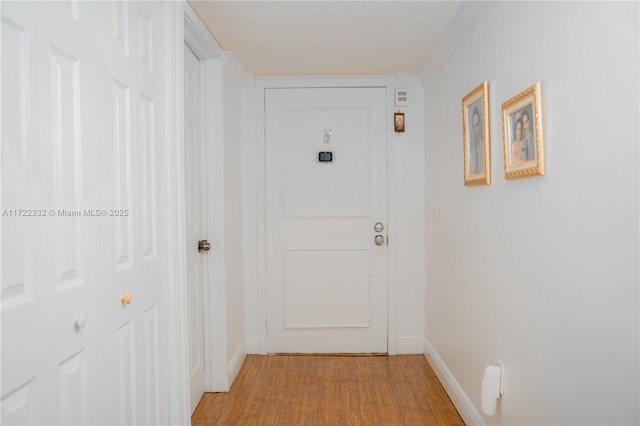 corridor featuring a textured ceiling, ornamental molding, and light hardwood / wood-style flooring