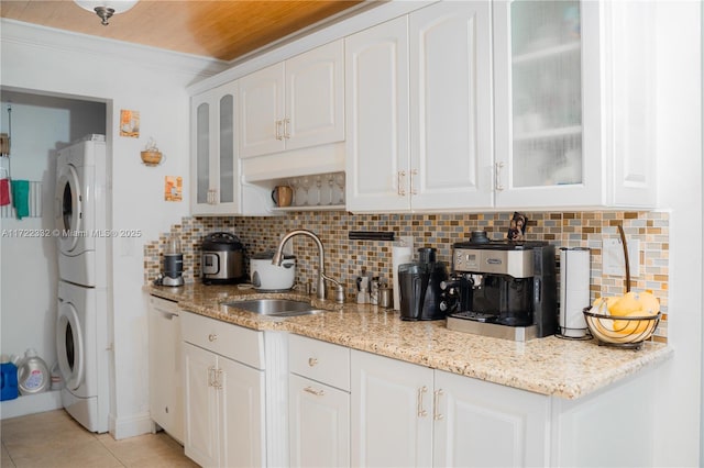 kitchen with white cabinets, stacked washer and dryer, backsplash, and sink